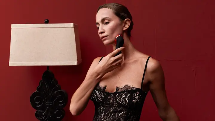 A beautiful woman in lingerie using FAQ 402 dual microcurrent device for skin tightening in a red room